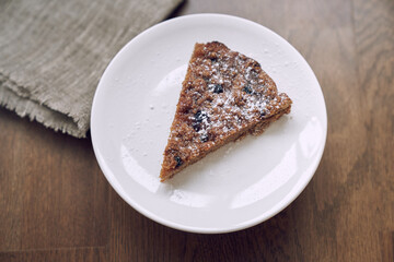 Part of the pie is on a white plate on the table. A piece of lemongrass with blueberries and cranberries without milk and eggs on flaxseed flour. The concept of healthy eating