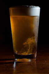 Tall Pint of Beer with foam head and bubbles churning in front of dark background. Chilled Pint Glass