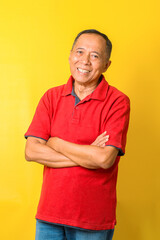 Portrait of Asian senior man wear red t-shirt with crossed arms isolated on yellow background.