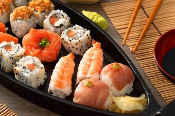 Japanese food and crispy onions served in restaurant on black boat on wooden table.