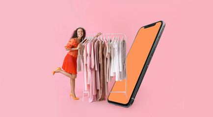 Stylish young woman with stylish clothes on hanger and modern mobile phone on pink background
