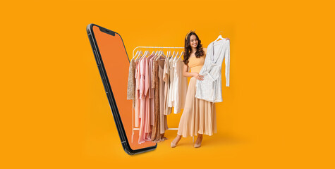Stylish young woman with stylish clothes on hanger and modern mobile phone on yellow background - obrazy, fototapety, plakaty