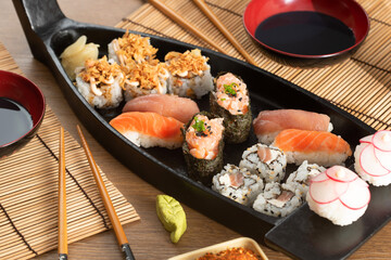 Japanese food and crispy onions served in restaurant on black boat on wooden table