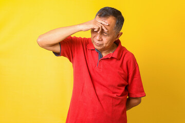 Fototapeta na wymiar Asian senior man wearing casual t-shirt over yellow background suffering from headache, hands on forehead.