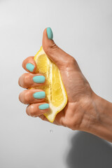 Hand with beautiful mint manicure squeezing lemon on light background