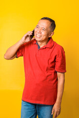 Portrait of happy Asian senior man talking on phone and smiling isolated over yellow background.