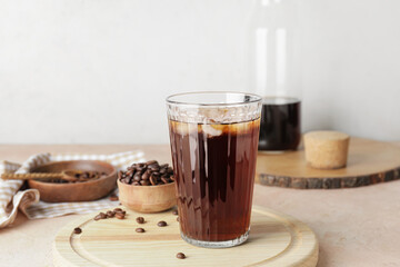 Glass with cold brew and coffee beans on wooden board against light background