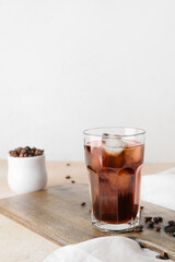 Wooden board with glass of cold brew and coffee beans on table against light background