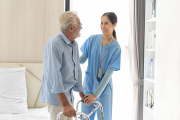 Female nurse caring senior man using walker in rehab center. Caregiver helping caucasian elderly...