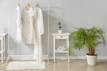 Rack with stylish female clothes, table and houseplant near light wall