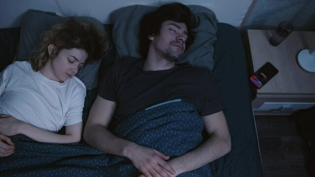  A couple sleeps in bed at night, the guy's alarm clock rings on the phone, the woman wakes up and nervously wakes him up. Slow motion 4k footage
