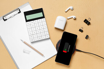 Mobile phone charging with wireless pad, earphones and stationery supplies on color background