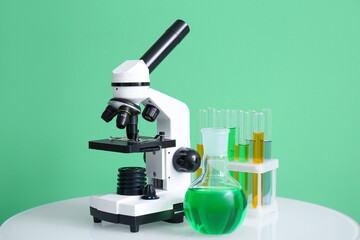 Modern microscope and laboratory glassware on table near green wall