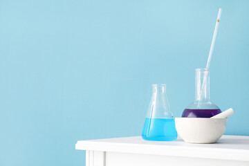 Different laboratory glassware on table near blue wall