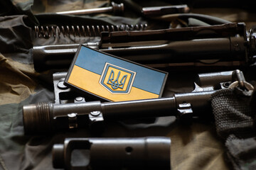 The patch of the flag of Ukraine lies on a disassembled machine gun on a green camouflage fabric,...