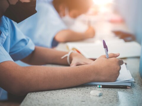 Student taking exam while wearing face mask due to coronavirus emergency. Young woman sitting in class with wearing surgical mask due to Covid-19 pandemic