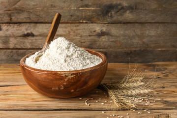 Bowl with flour and wheat ears on wooden background