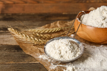 Sieve and bowl with wheat flour on wooden background