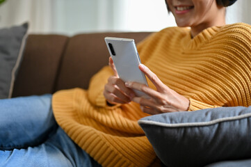 Female lying leaning on comfortable sofa and using her phone to chat with her friends