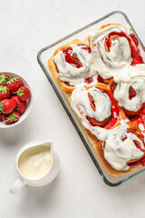Baking dish with strawberry cinnamon rolls and cream on white background
