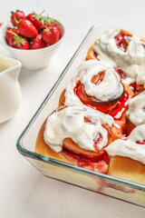 Baking dish with strawberry cinnamon rolls and cream on white background, closeup