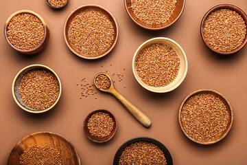 Wooden bowls and spoon with buckwheat grains on color background