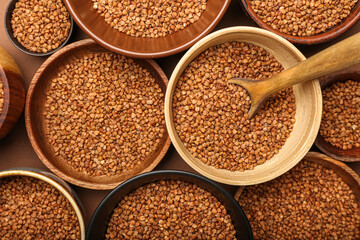 Wooden bowls and spoon with buckwheat grains on color background, closeup