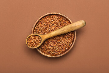 Bowl and spoon with buckwheat grains on color background