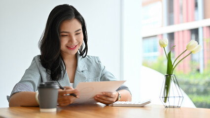 Asian businesswoman reviewing a business proposal report, analysing financial document - obrazy, fototapety, plakaty