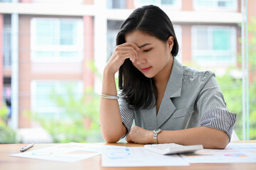 Stressed asian businesswoman worried about her work, suffering from headache