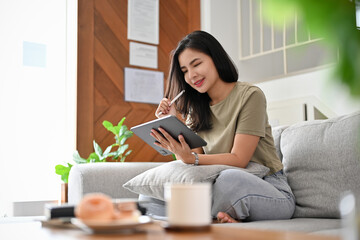 Beautiful young asian woman relaxes in the living room using digital tablet.