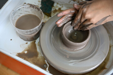 Fototapeta na wymiar A female hands making a ceramic cup on potter's wheel in the clay handicraft workshop.