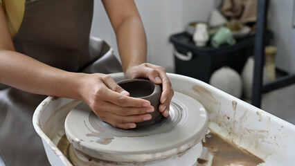 Woman potter hands making a ceramic cup on potter's wheel, moulding clay