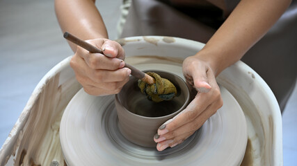 A female hands using a scrapper, making a ceramic cup on potter's wheel.