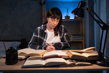 Female student reading book, prepare for exam at table at night. Education