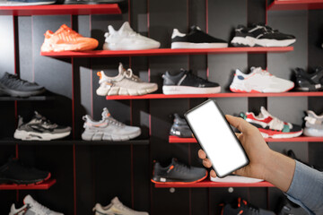 smartphone with sport shoes on shelves in sneakers shop modern sports store background. mobile phone with blank screen for your advertisment. business concept.