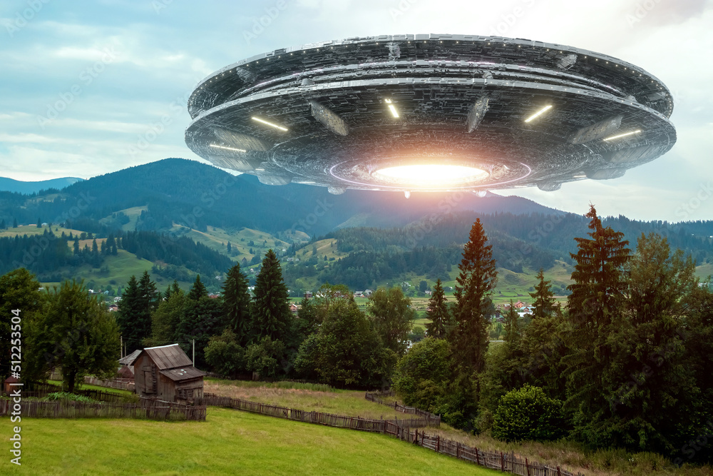 Wall mural ufo, an alien saucer hovering above the field in the clouds, hovering motionless in the sky. unident