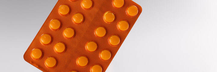 Orange blister with pills on gray background.