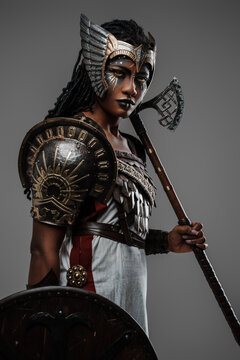 Shot of isolated on grey black woman warrior holding axe and shield dressed in ancient armor.