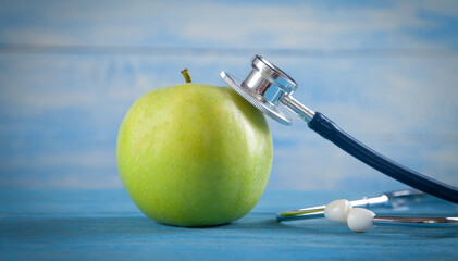 Green apple with stethoscope on the blue background.
