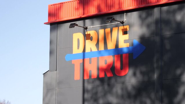 Orange-painted "DRIVE THRU" signage painted on a building's wall in gray and arrow pointing towards the right to the direction of drive through.