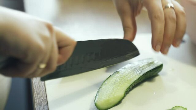 A woman cuts a cucumber into strips. Close-up. Holds a cucumber and cuts it lengthwise with a knife.