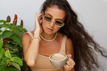 Stylish woman in  summer crop top and  straw skirt drinking coffe in  modern cafe.  Enjoing summer vacations in Europe.