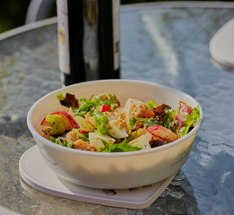 Bowl of summer salad outside on a table with a bottle in the background.