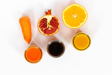 three kinds of juices orange, pomegranate, carrot on a white surface, carrot and orange slices, pomegranate seeds, top view, healthy food concept, vitamin detox, diet