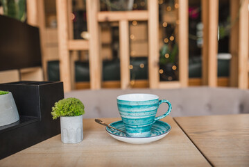 Blue vintage coffee cup on wooden table in a cafe. Stabilized moss decorations in vase 