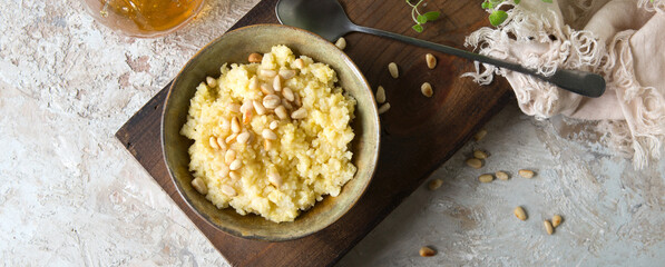 a bowl of millet porridge with honey and pine nuts on the table - obrazy, fototapety, plakaty