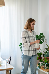 Woman spraying houseplant at home, she is caring about her plants. Florist take care of domestic flowers, pour liquid, fertilize, enrich dry ground, horticulture, gardening concept.
