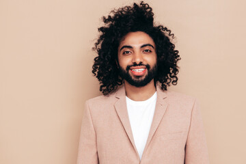 Handsome smiling hipster  model.Unshaven Arabian man dressed in elegant beige suit . Fashion male with long curly hairstyle posing near beige wall in studio. Isolated