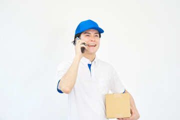 段ボール箱を持ってスマホで話すキャップとポロシャツのユニフォームの男性　白背景